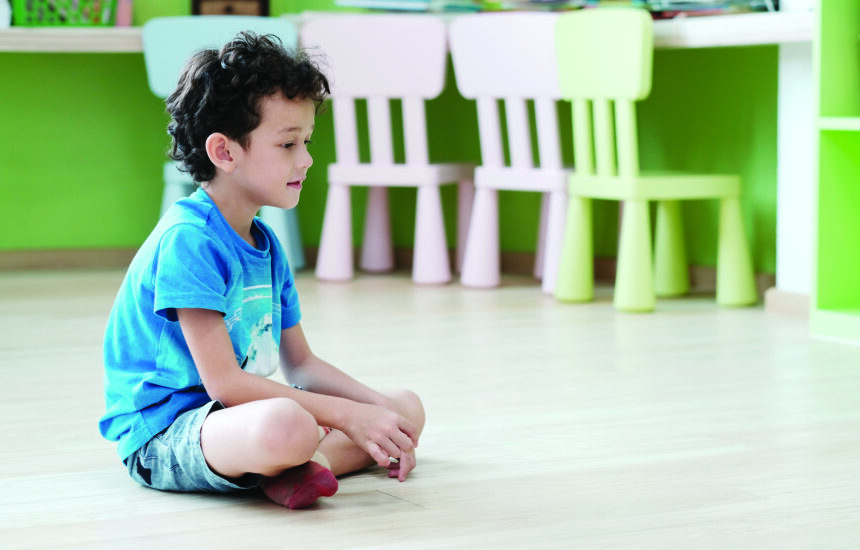 A young boy sitting cross-legged on the floor of a classroom