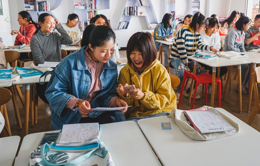 Photo of teenagers in a school classroom, engaging in conversation with one another.