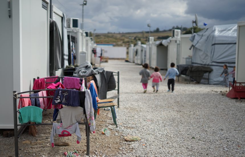 Temporary buildings in a refugee camp, with clothes hanging to dry and children walking in the distance