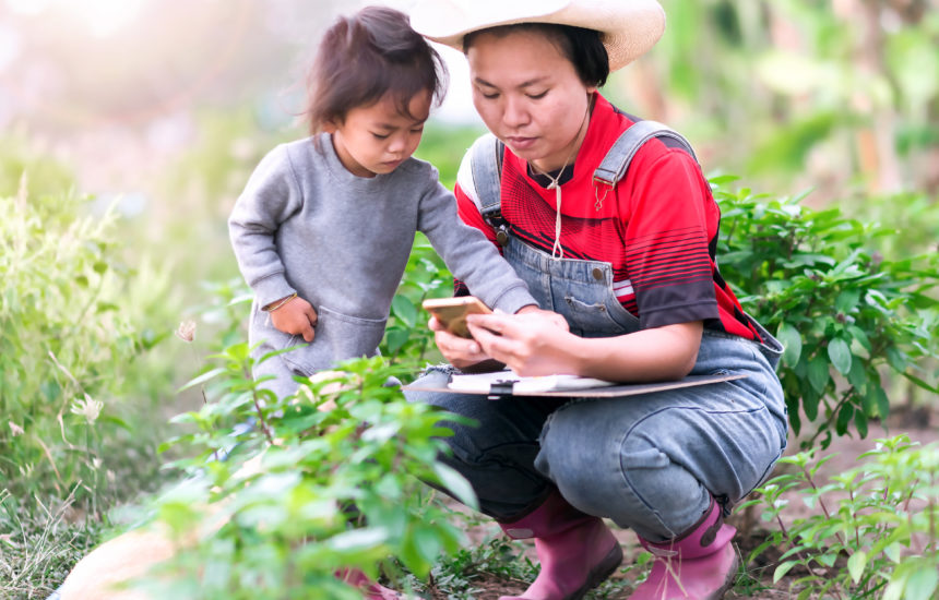 A woman and a child are gardening and looking at a phone for help