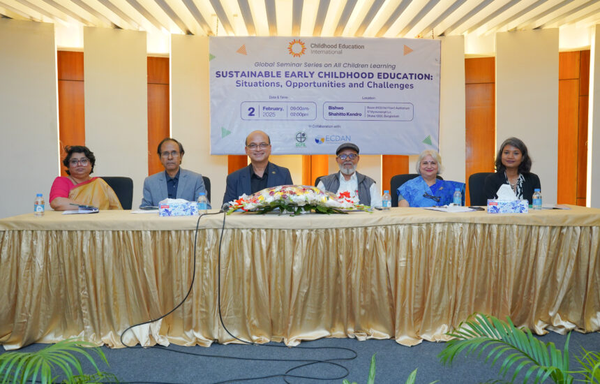 Six presenters at the global seminar, seated behind a table at the front of the presentation room, with a seminar banner behind them.