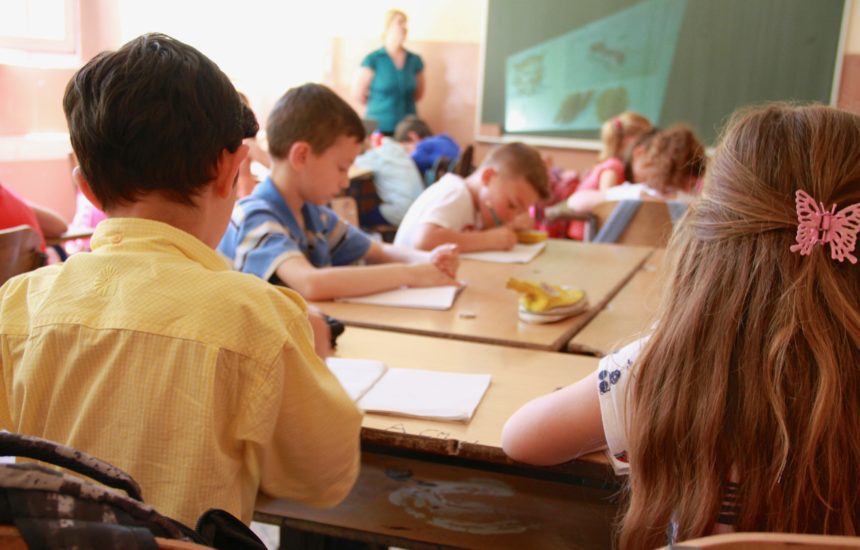 A classroom in Serbia with young children sitting at desks and a teacher standing in the distance