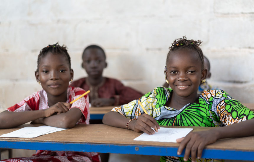 Children sitting at tables writing and smiling