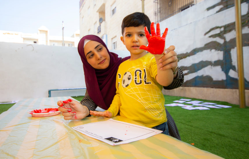 A woman holds up a young boys hand that has red paint on it