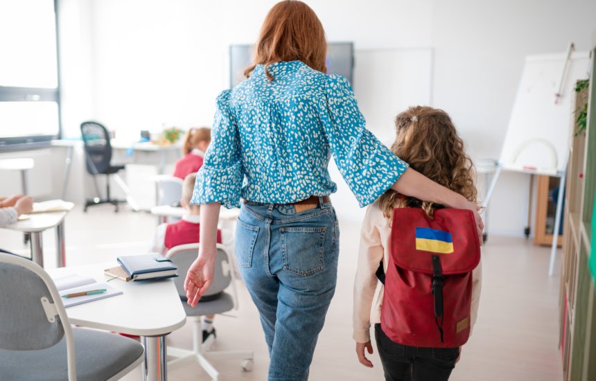 Teacher with her arm around a student wearing a backpack with the Ukrainian flag on it, walking away from the camera