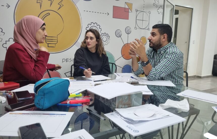 Three teachers sitting together in a classroom, talking and sharing their experiences.