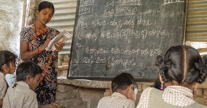 A teacher teaching children in front of a chalkboard