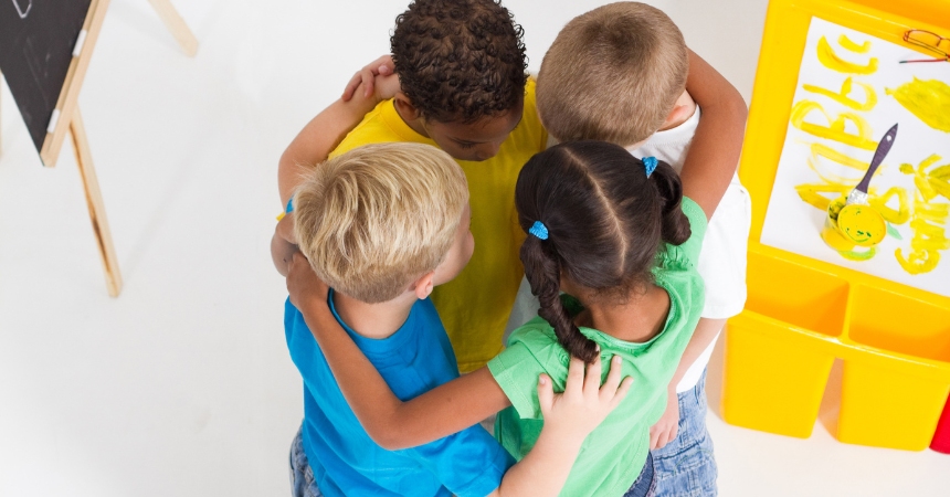 Four children standing together in a huddle in a classroom.