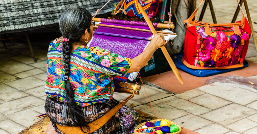 A woman in Guatemala sitting on the ground, weaving a colorful tapestry