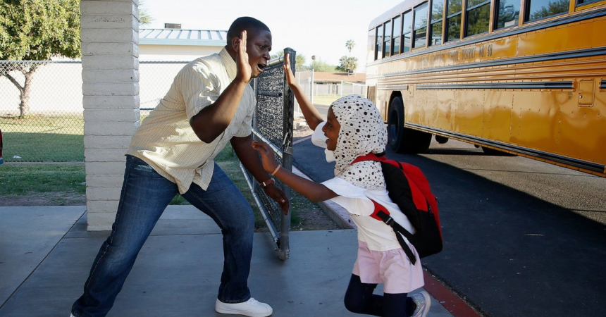An energetic teacher holding out his hand for a high-five with a happy young student getting off a bus at school.