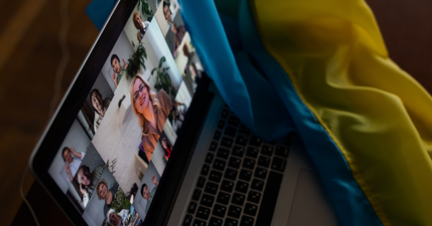 A laptop with video squares of multiple people at an online training. Next to the laptop is the Ukrainian flag.