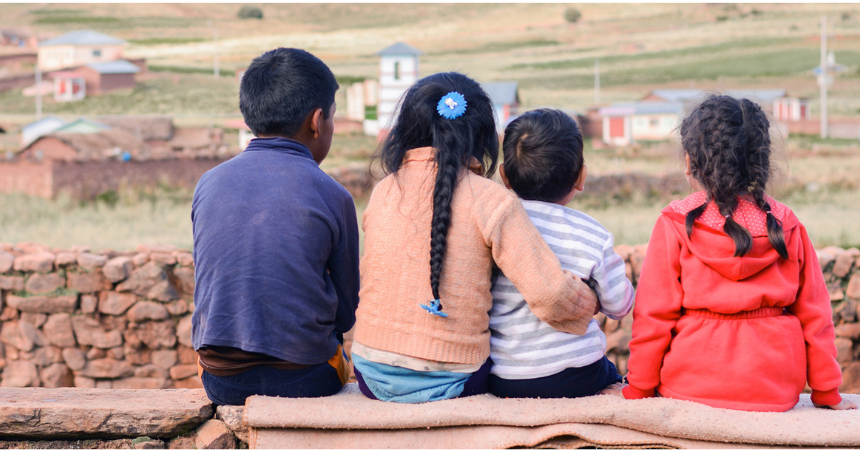 Photo of four children with their backs to the camera, looking out at the scene. One has her arm around another