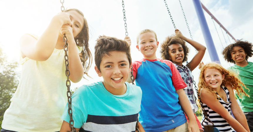 Five children happily playing together on a swingset outdoors